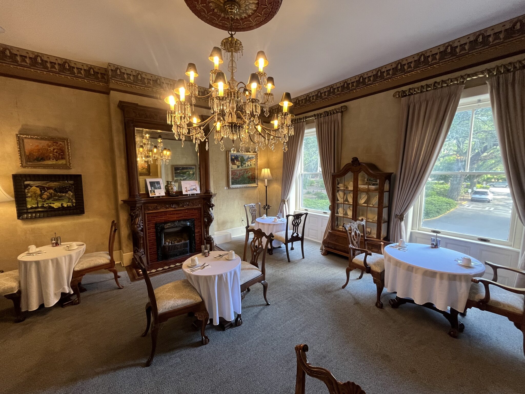 A formal dining room with a chandelier, fireplace, and round tables set with white tablecloths.